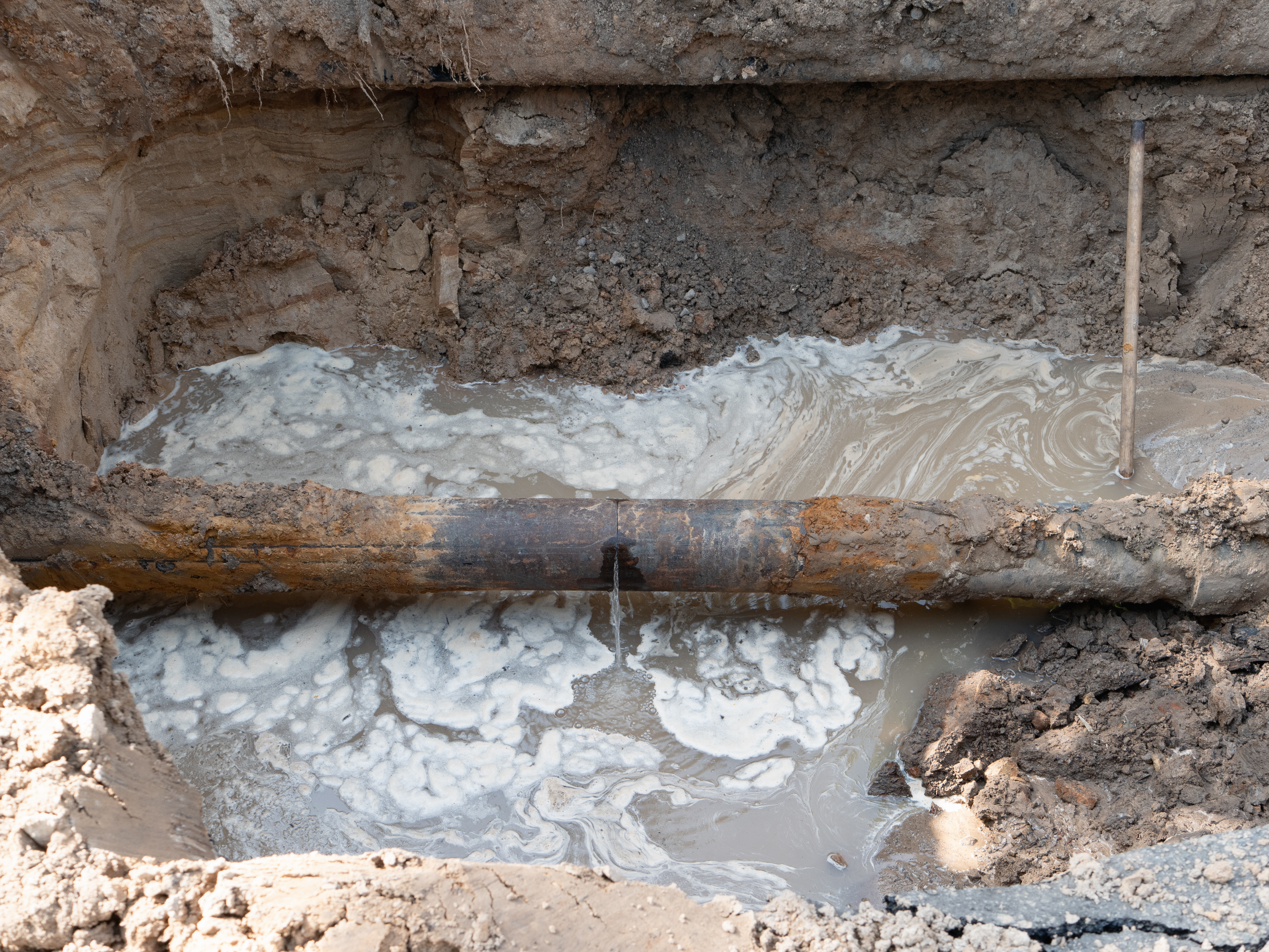 A severely corroded underground pipe with a large hole broken clear through the wall