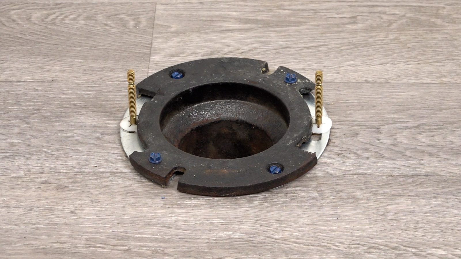 Cast iron toilet flange repaired with Fernco Fix-A-Flange horseshoes screwed to the floor, with brass toilet bolts in place